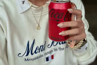 Woman sipping a Coca-Cola through a straw while wearing a cream “Mont Blanc” sweatshirt — a quiet, grounded moment that reflects the everyday rhythm of becoming her and living out simple, intentional habit ideas.